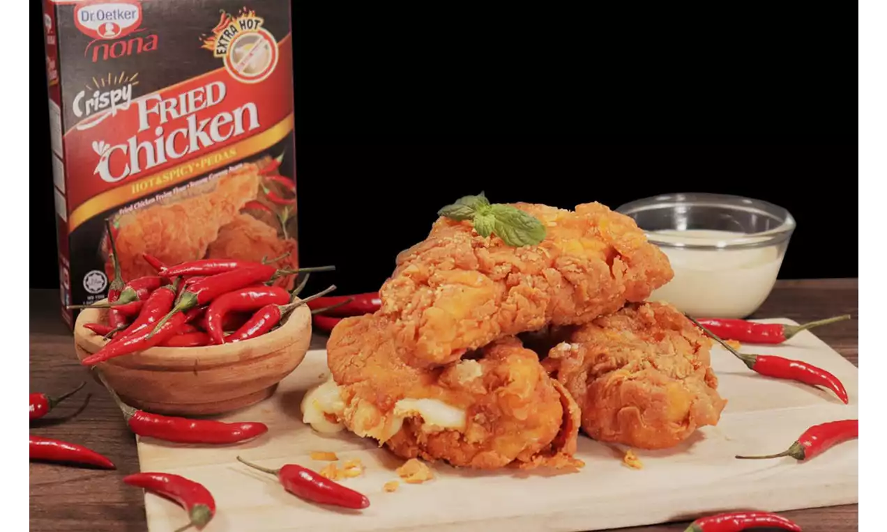 Golden-brown crispy fried chicken pieces with melted cheese oozing out, garnished with a mint sprig, surrounded by red chilies on a wooden board