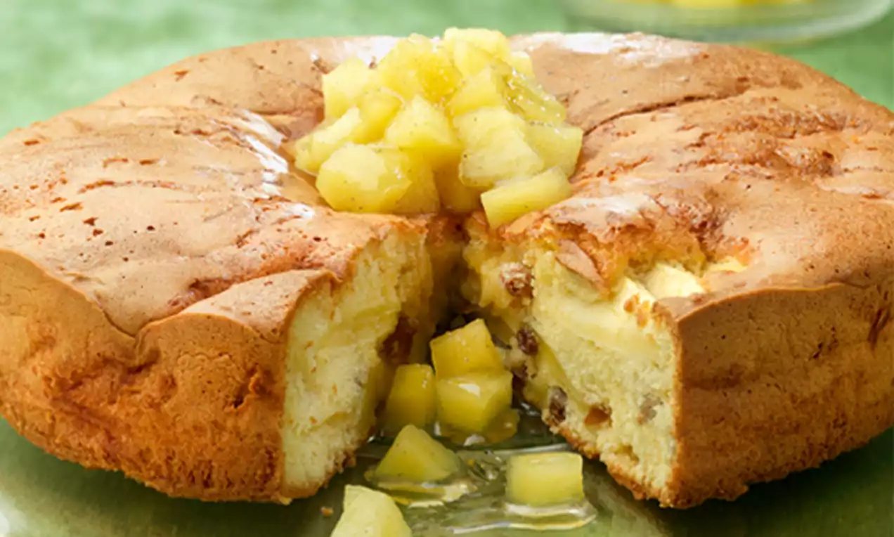 Pastel dorado con textura esponjosa relleno de trozos de manzana y canela, coronado con cubos brillantes de manzana en almíbar