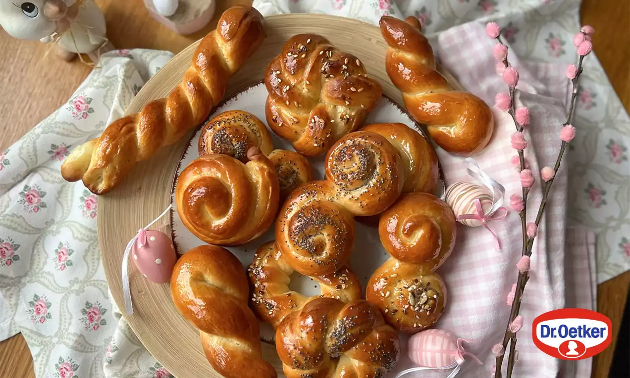 Lesklé zlatisté medové judáše rôznych zakrútených tvarov, posypané makom alebo semienkami, na drevenom tanieri obklopenom jarnými dekoráciami