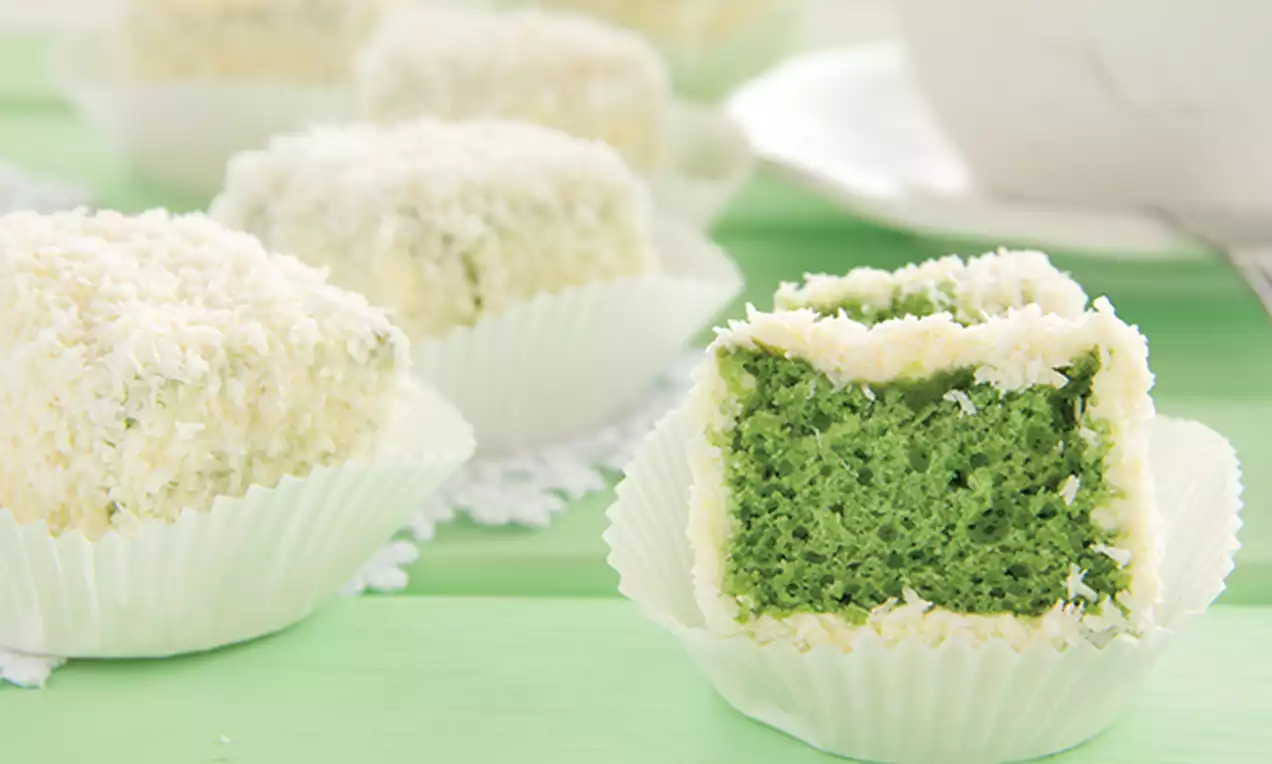 Moist emerald green cake cubes with soft texture, coated with snowy white shredded coconut in paper cups on a light green surface