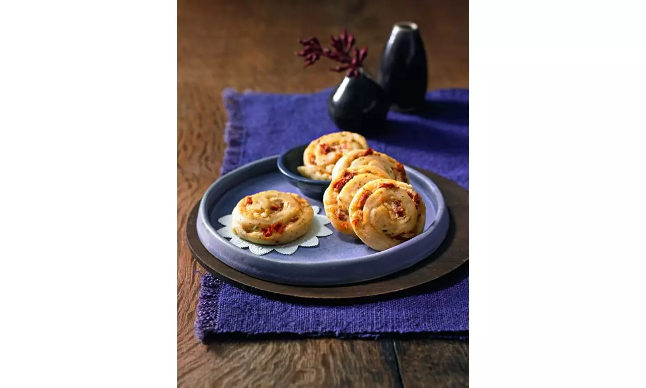 Melci aurii din aluat dospit, rulați cu ingrediente mediteraneene, așezați pe o farfurie albastră, pe un șervet mov, cu decor minimalist