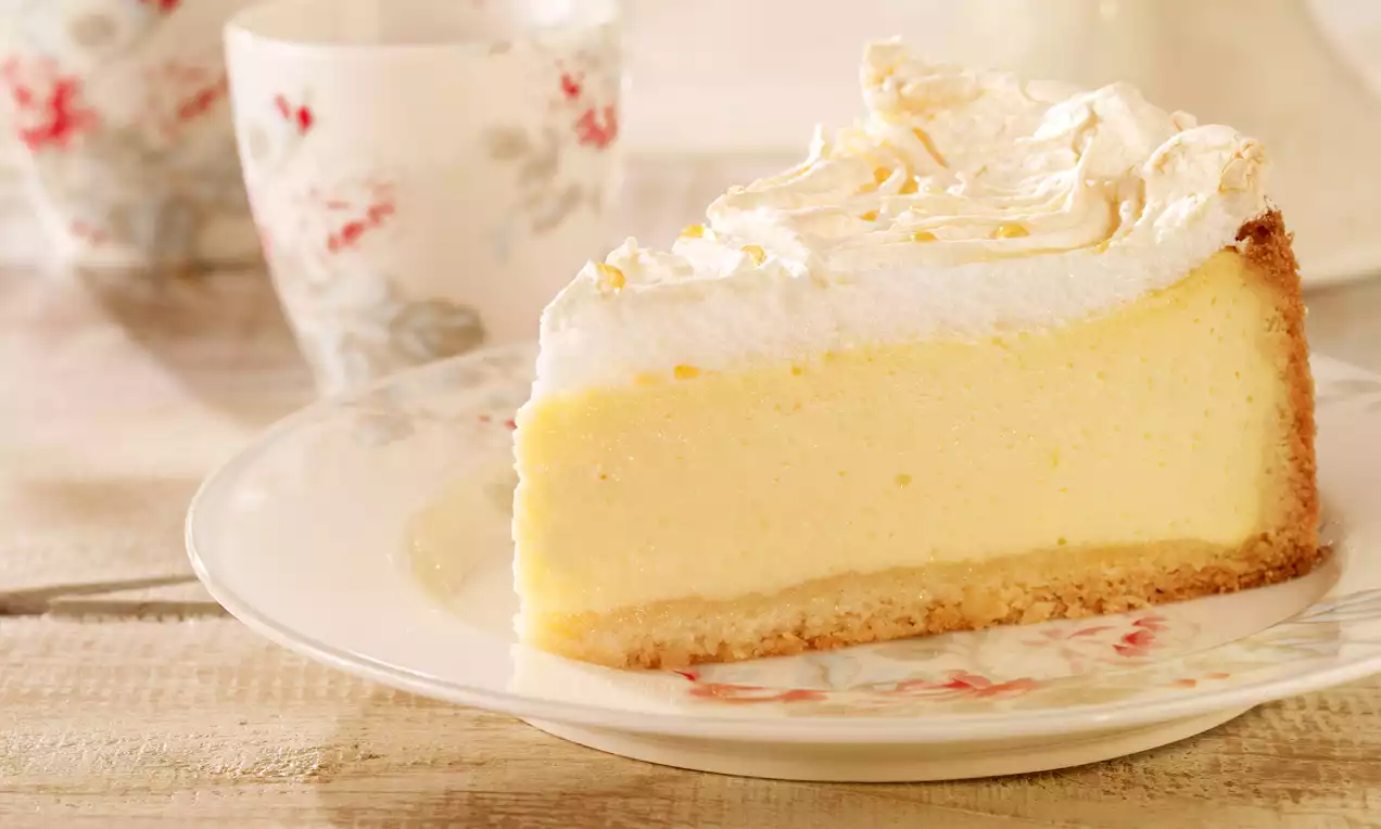 Kriška svijetložute kremaste torte na zlatnosmeđoj podlozi, prekrivena bijelim slojem pjenastog šlaga, na ukrasnom tanjuru s cvjetnim motivom