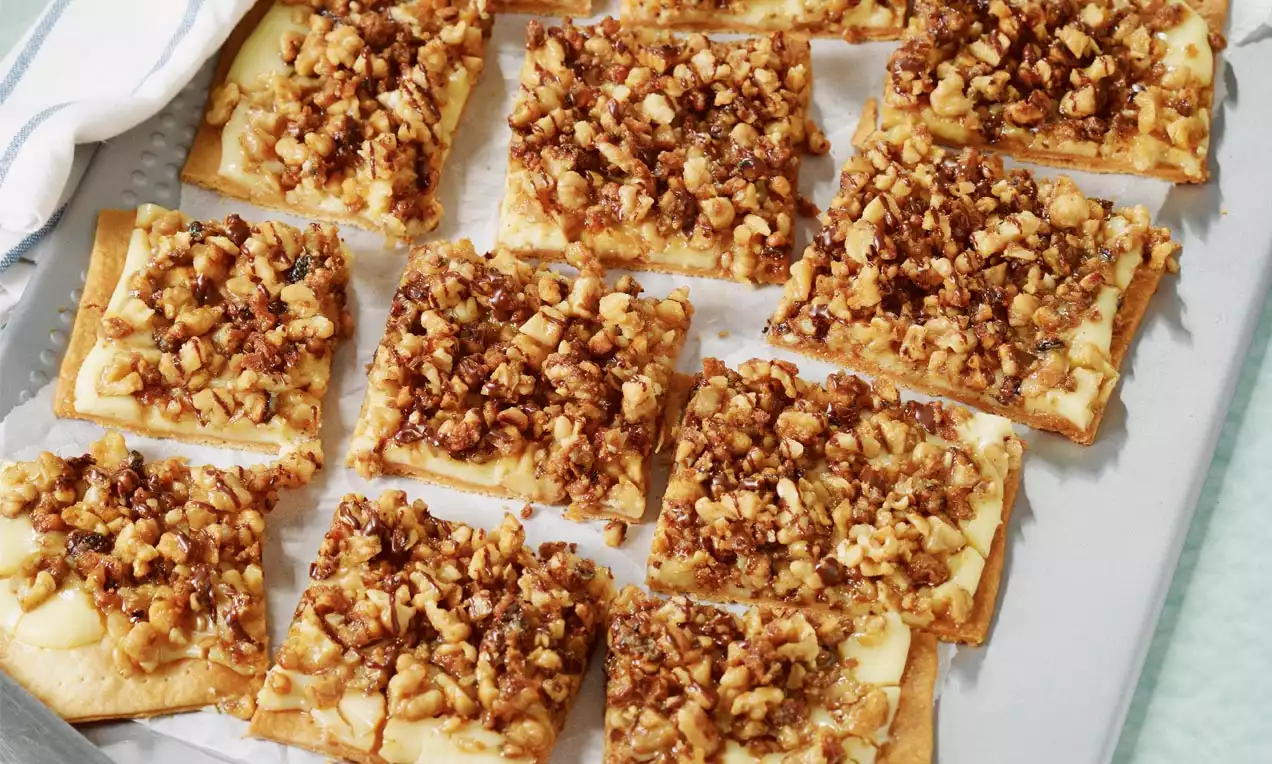 Goldene Teigstücke mit karamellisierten Nüssen dicht bedeckt, in rechteckigen Portionen auf Backpapier und einem Blech angerichtet