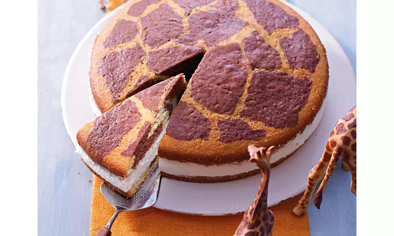 Runder Kuchen im Giraffenmuster mit dunklen und hellen Flecken, gefüllt mit heller Creme, ein Stück auf einem Tortenheber, kleine Giraffenfiguren