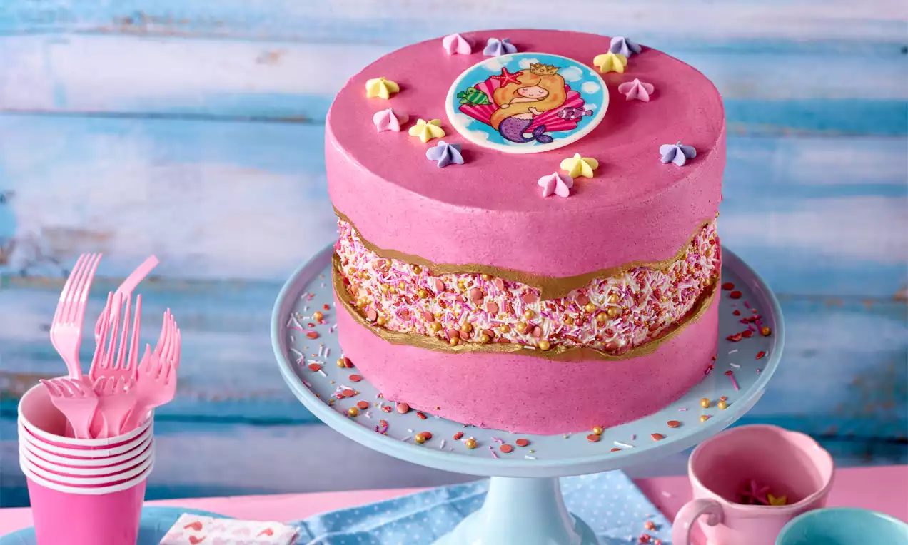 Rosa Meerjungfrau-Torte mit zweischichtigem, goldumrandetem Kern aus bunten Streuseln, dekoriert mit Sternen und einem Meerjungfrau-Topper