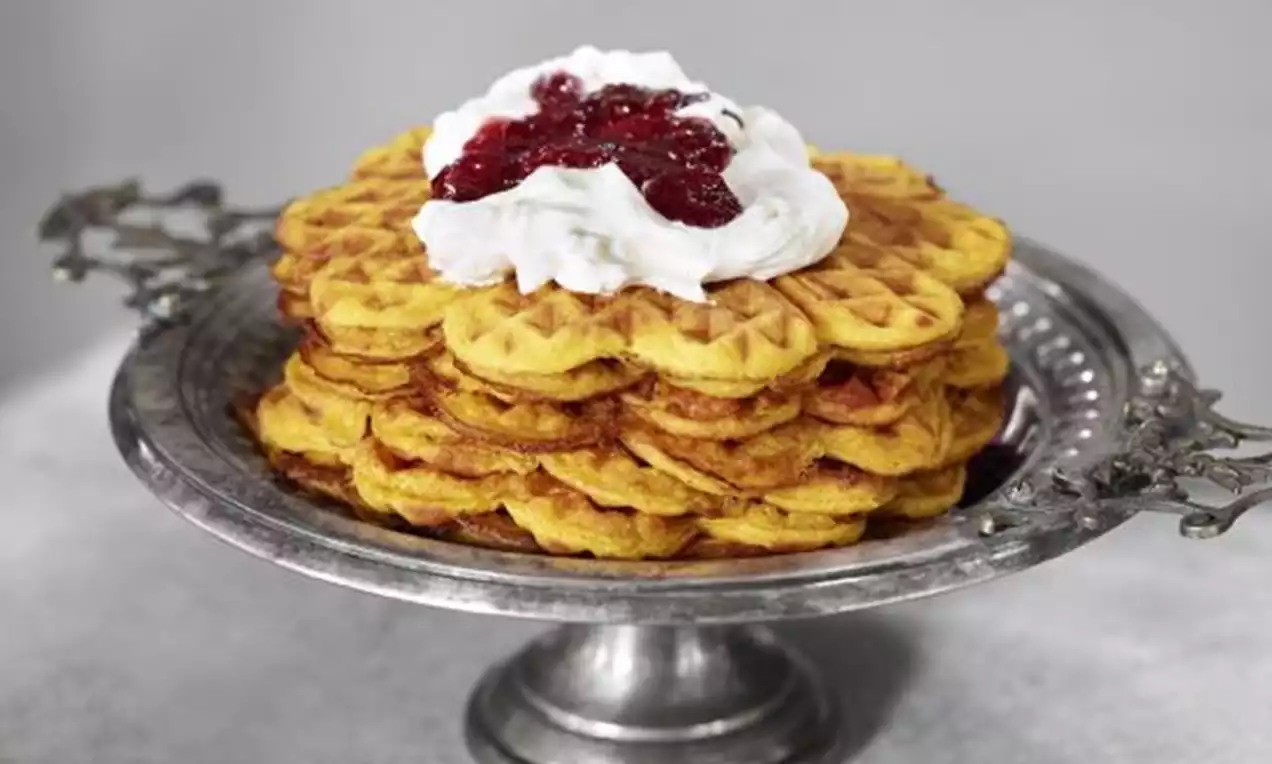 Gyllengula våfflor med tydlig rutmönster, toppade med vit grädde och röd sylt, upplagda på ett dekorativt silversfat