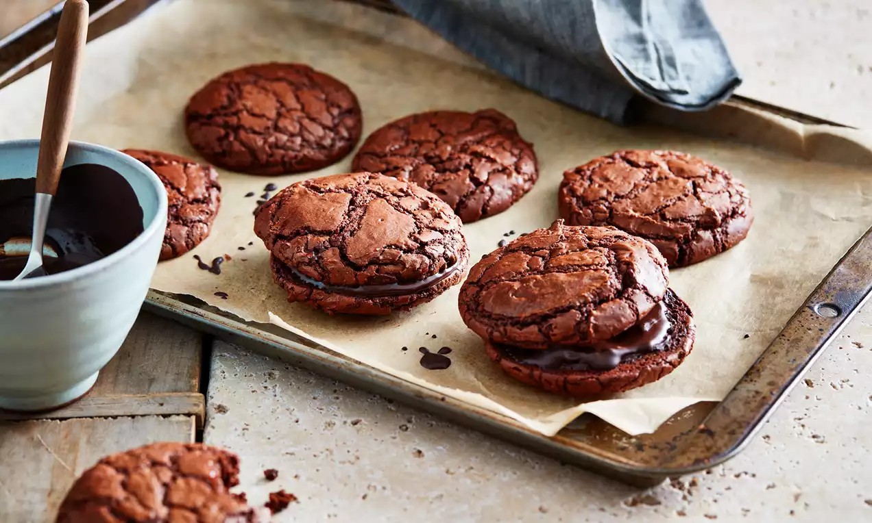 Chocolate brownie cookies met diepe barstjes en een glanzende chocoladevulling, gepresenteerd op bakpapier op een metalen bakplaat