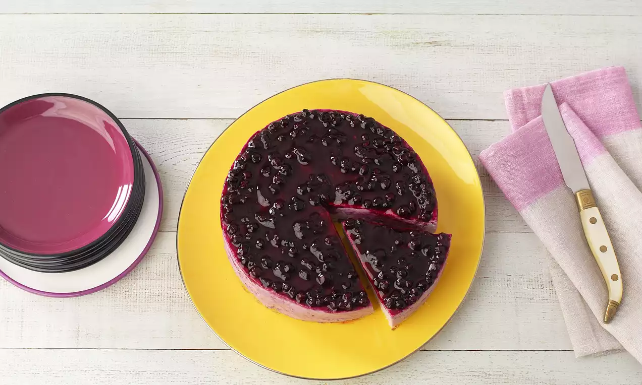 Yuvarlak sarı tabakta frambuaz kırmızısı katmanlı ve parlak mor yaban mersini sosuyla kaplı soğuk pasta dilimlenmiş şekilde