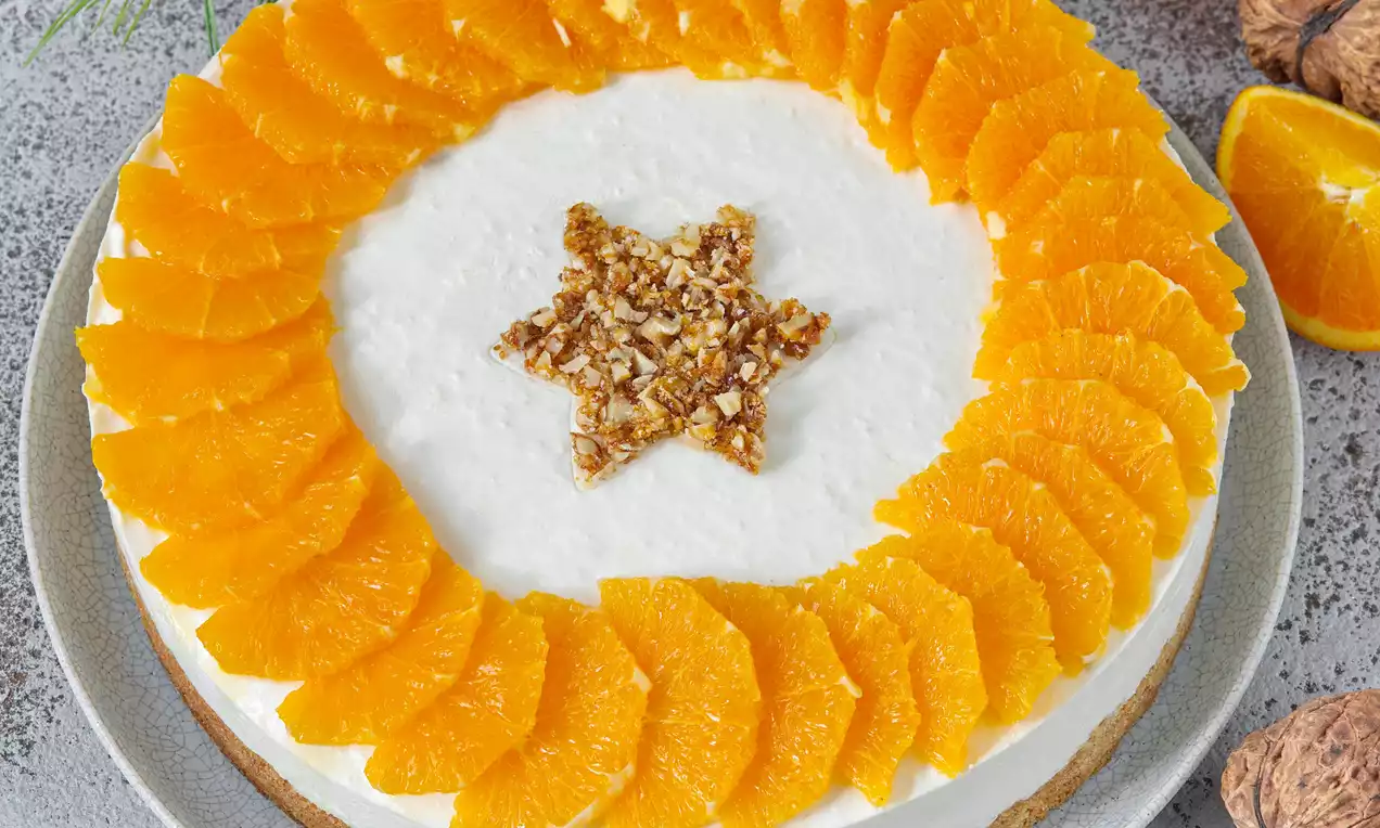 Kulatý pomerančový dort se sněhově bílým povrchem, lemovaný plátky zářivě oranžového pomeranče, uprostřed hvězda z drcených ořechů