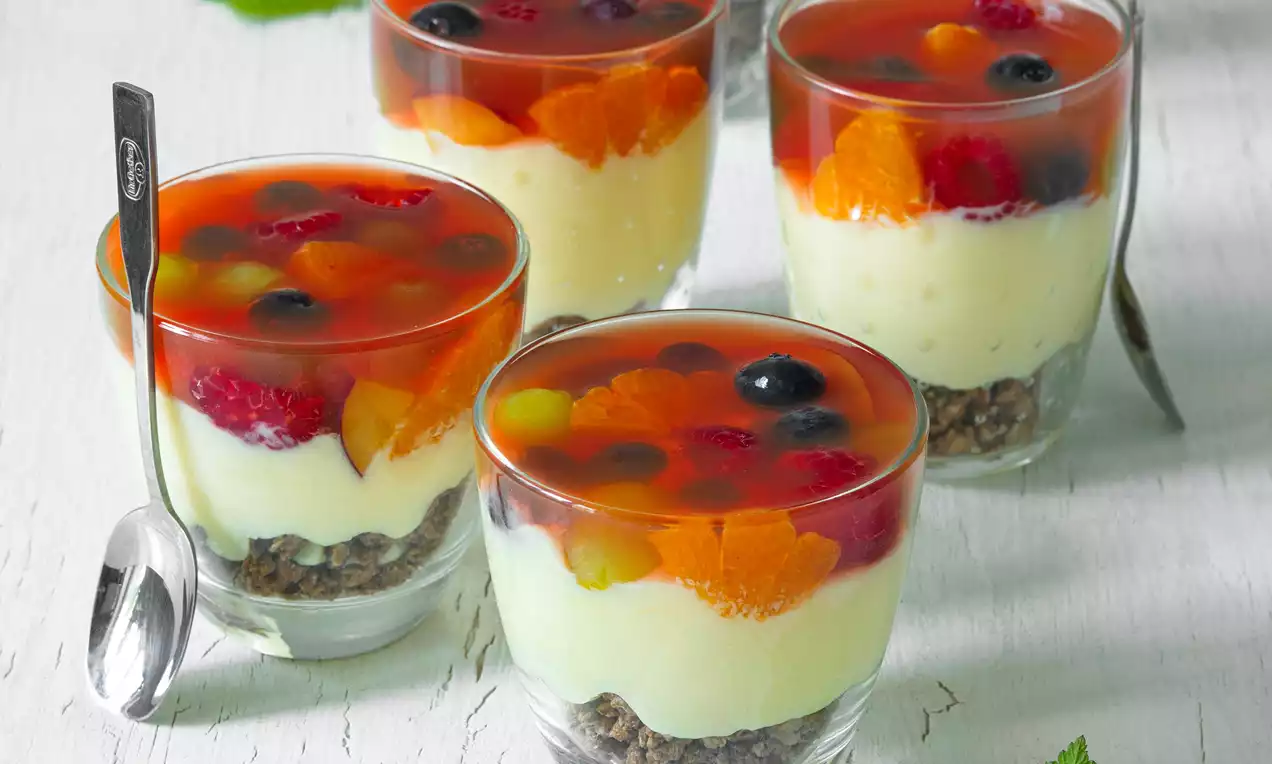Pudingový dezert vo vysokom sklenom pohári s vrstvou smotanového pudingu, ovocím ponoreným v želé a chrumkavým kakaovým základom