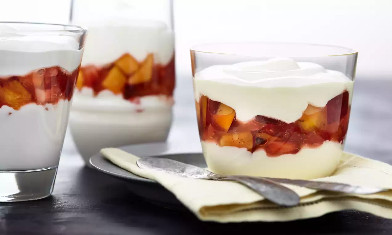 Dessert in bicchieri di vetro con strati cremosi bianchi di quark, frutta fresca arancione e rossa e morbida crema bianca decorativa