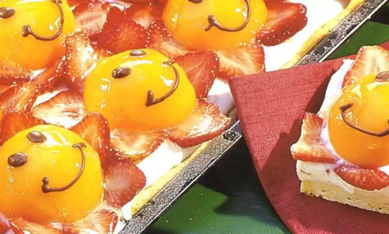 Dômes glacés à l’abricot orangé garnis de sourires au chocolat, entourés de fines tranches de fraises rouges sur une base biscuitée