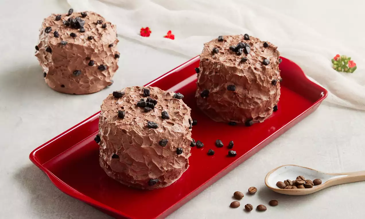 Kahverengi kahve kremasıyla kaplı, yuvarlak, pürüzlü yüzeyli, üzeri kahve çekirdeği parçalarıyla süslenmiş tatlılar kırmızı tabakta