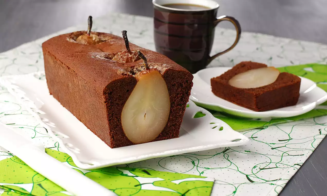 Kakao renkli dikdörtgen kek içinde bütün armutlarla süslenmiş, dilimlenmiş keki yanında kahveyle beyaz tabakta sunulmuş