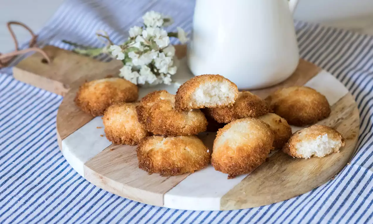 Galletas doradas de coco con textura crujiente por fuera y suave interior blanco dispuestas sobre tabla de madera con fondo rayado azul