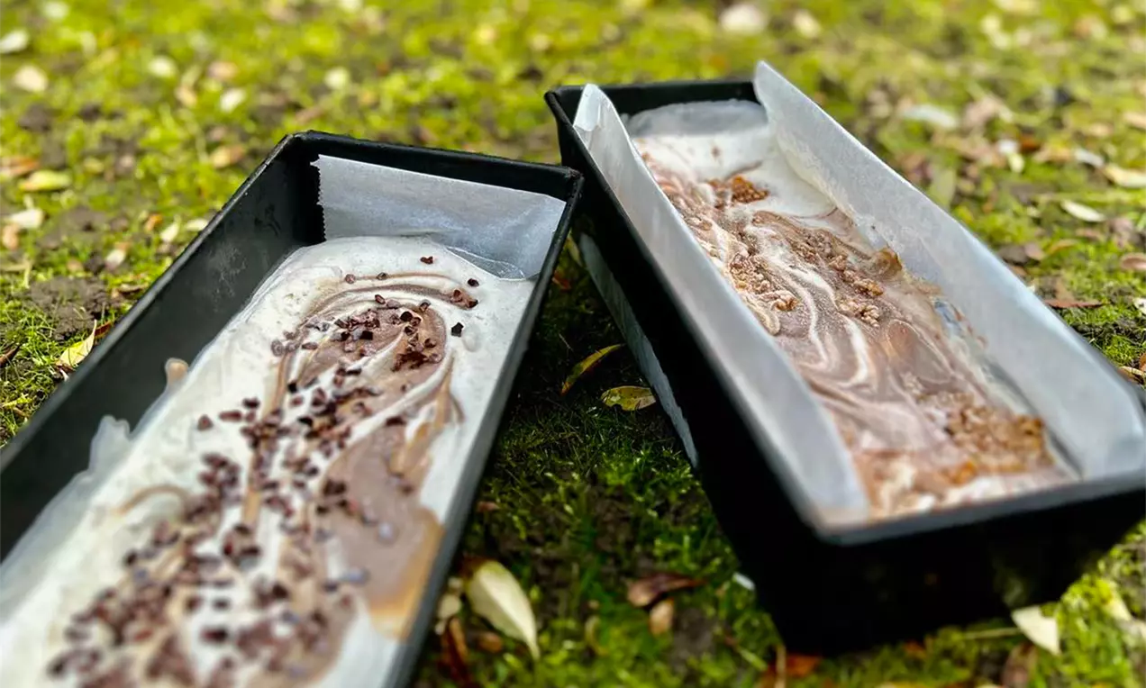 To aflange sorte forme med is i marmorfarver dekoreret med små chokoladestykker placeret på en mosbeklædt flade