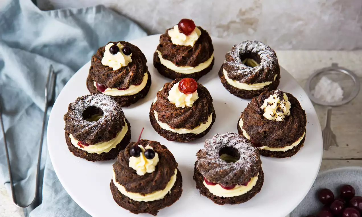 Makovo-orechové mini bábovky tmavohnedej farby s jemnou štruktúrou, plnené vanilkovým krémom, ozdobené drobným ovocím na bielom tanieri