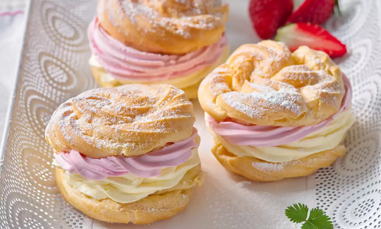 Zlatisté veterníky plnené jemnou žltou a ružovou šľahačkovou náplňou, posypané práškovým cukrom na ozdobnom tanieri so sviežimi jahodami