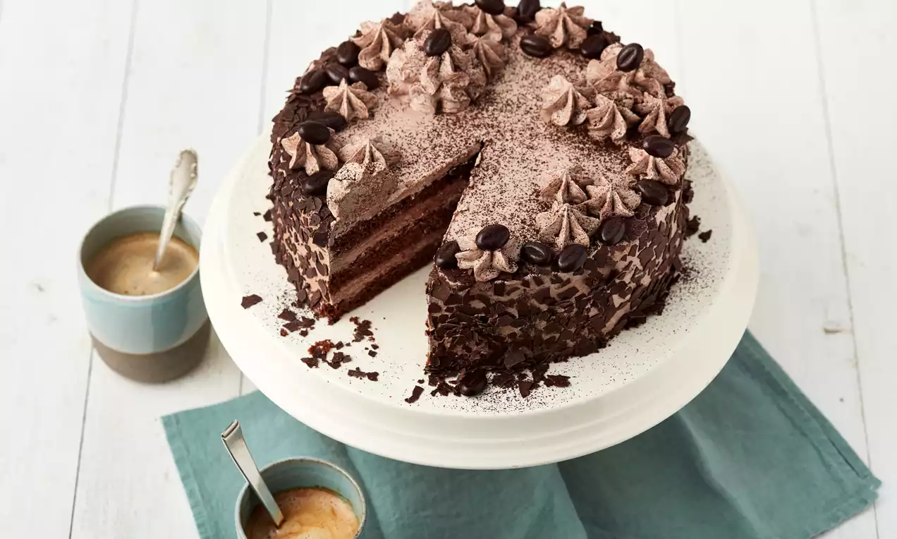 Mokka-Torte mit Schokoschichten, bestäubt mit Kakaopulver, garniert mit Sahnetupfen und Kaffeebohnen auf weißer Tortenplatte