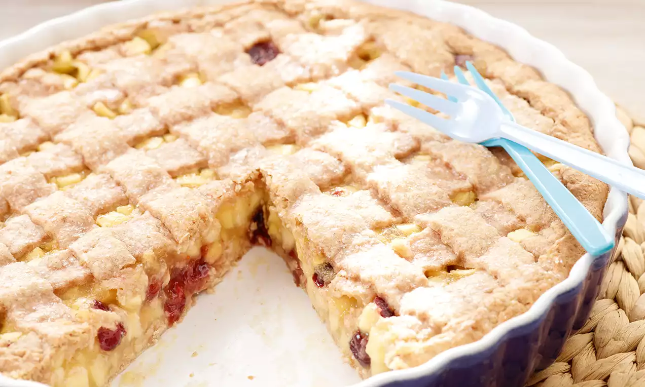 Apfel-Dinkel-Pie dalla crosta dorata intrecciata, ripieno di mele e frutti rossi morbido e lucido, servita in una teglia bianca