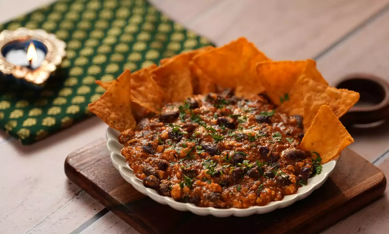 Paneer and beans stir fry in a white fluted bowl, rich red-orange hues, topped with chopped green herbs, surrounded by crisp golden chips