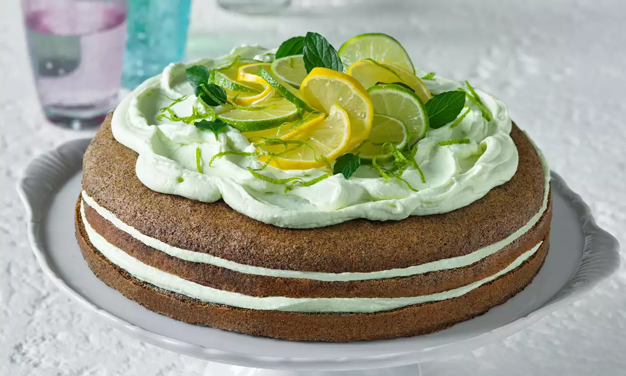 Makový tort s dvoma vrstvami jemného cesta, limetkovo-citrónovou plnkou a lístkami mäty, zdobený kolieskami citrónu a limetky na bielom podnose