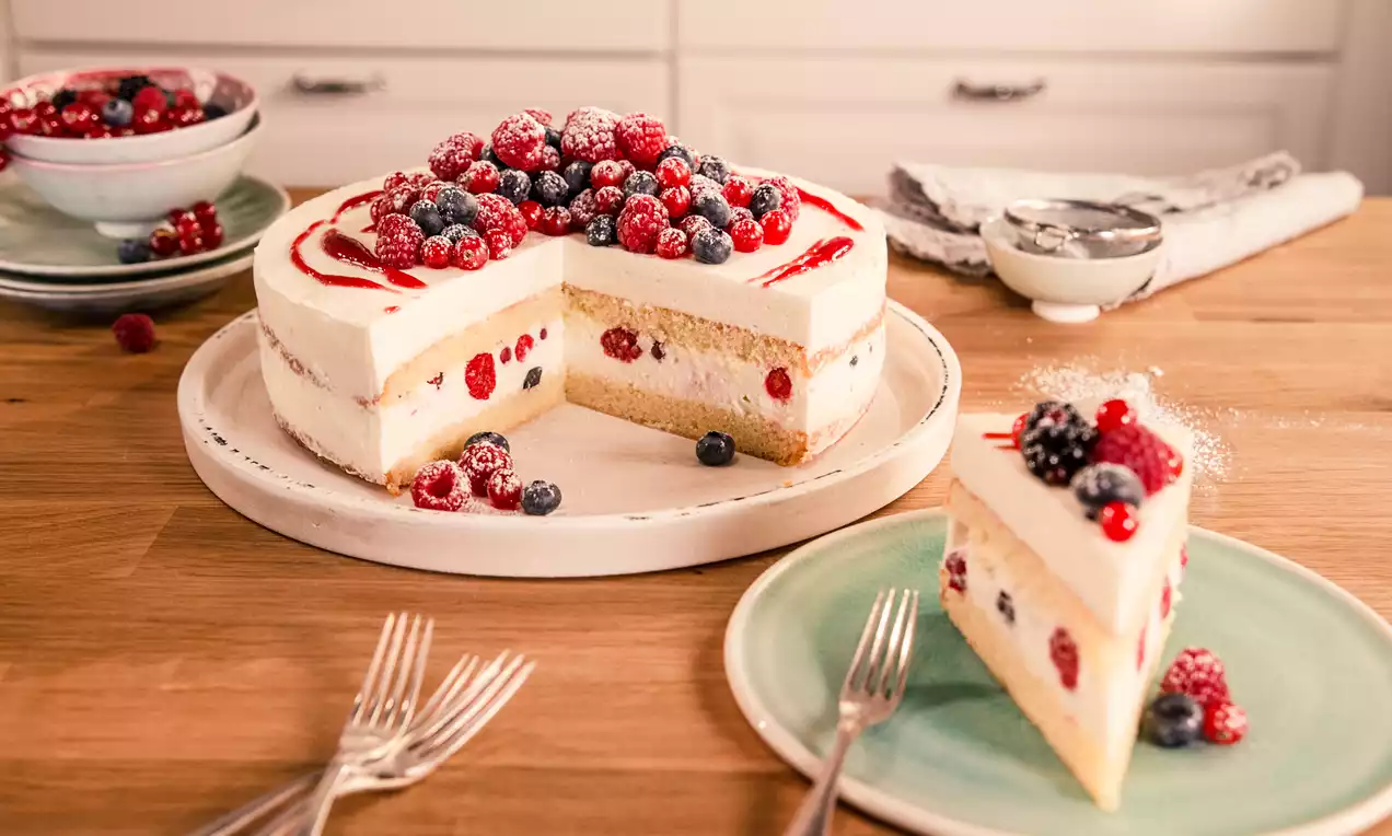 Beerige Käse-Sahne-Torte mit weißer Creme auf hellem Boden und roten sowie blauen Beeren, leicht bestäubt auf einer weißen Platte