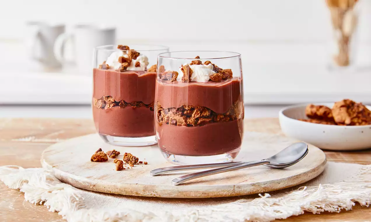 Cam bardakta sunulan çikolatalı puding, aralarına serpiştirilmiş gevrek kek parçaları ve üzerine eklenmiş köpük benzeri hafif beyaz krema