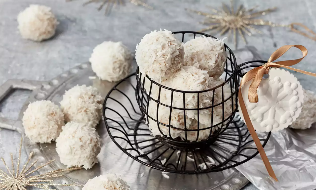 Schneebälle mit Kokosraspeln, goldbraun und weiß bestäubt, auf einem dunklen Teller gestapelt, dazu ein Zweig Minze
