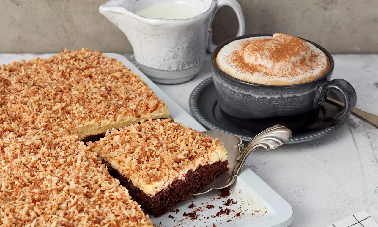 Mit diesem Rezept gelingt ganz einfach der beliebte Blechkuchen mit saftigem Schokoboden, Vanillecreme und knusprigen Kokos-Raspeln.