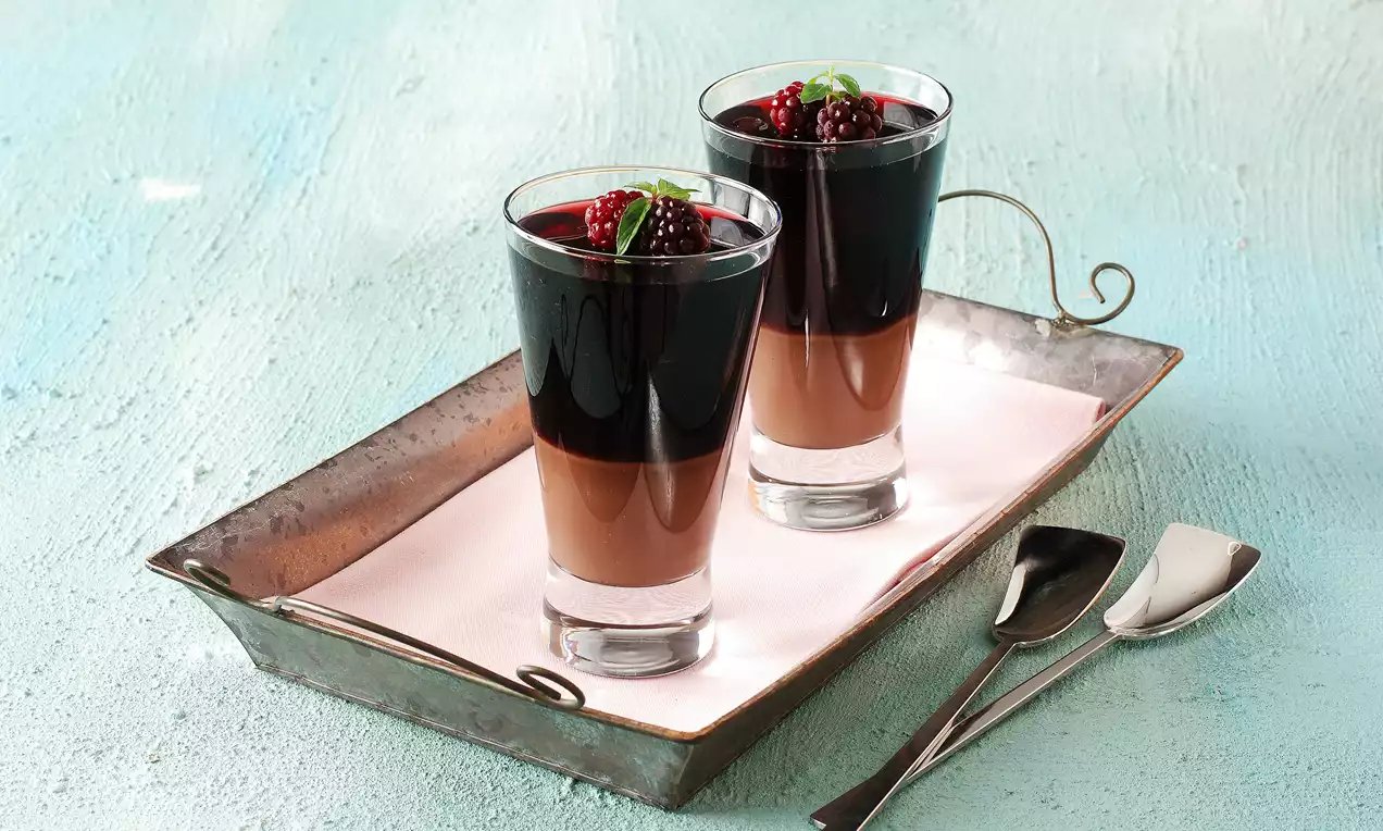 Cam bardaklarda katmanlı sunulan çikolatalı mousse, üzeri koyu böğürtlen sosu ve taze böğürtlenlerle süslenerek metal tepside servis edilmiş