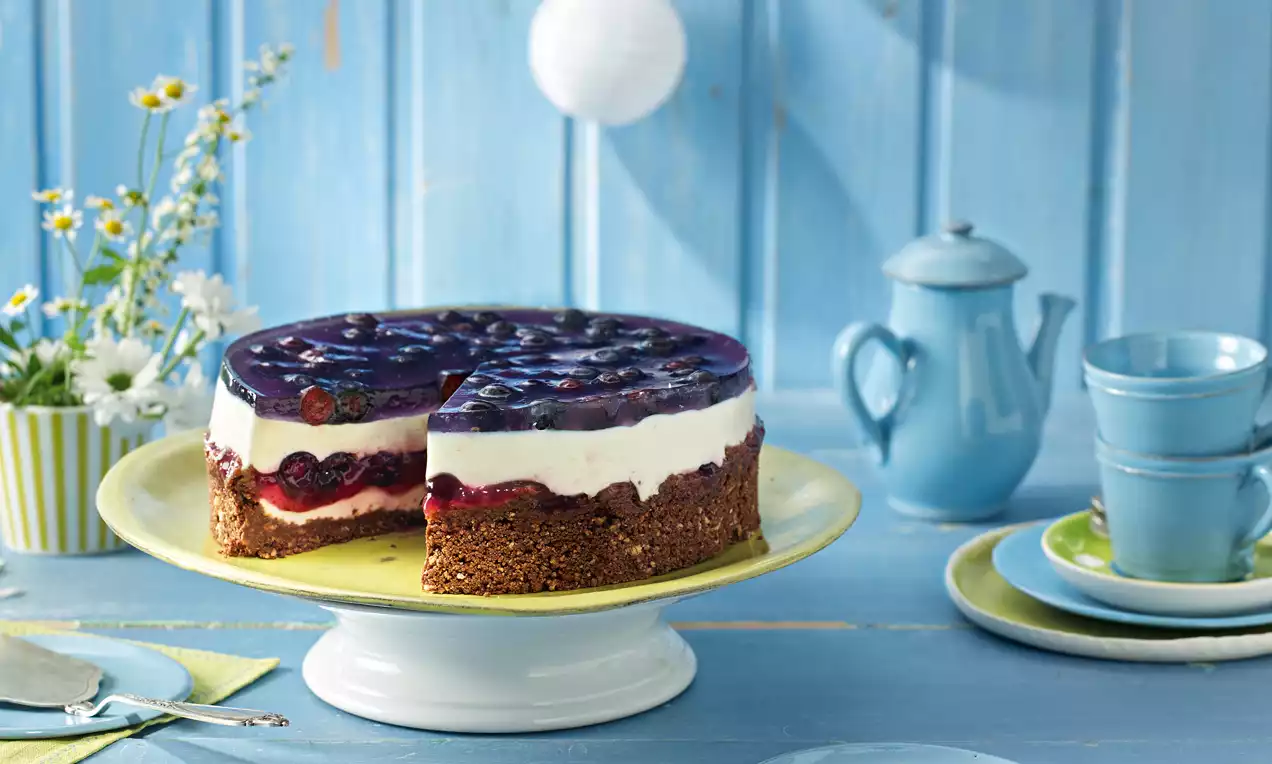 Kleine Heidelbeer-Joghurt-Torte mit cremiger weißer Joghurt-Schicht, dunkelblauem Heidelbeeren-Topping und schokoladigem Keksboden