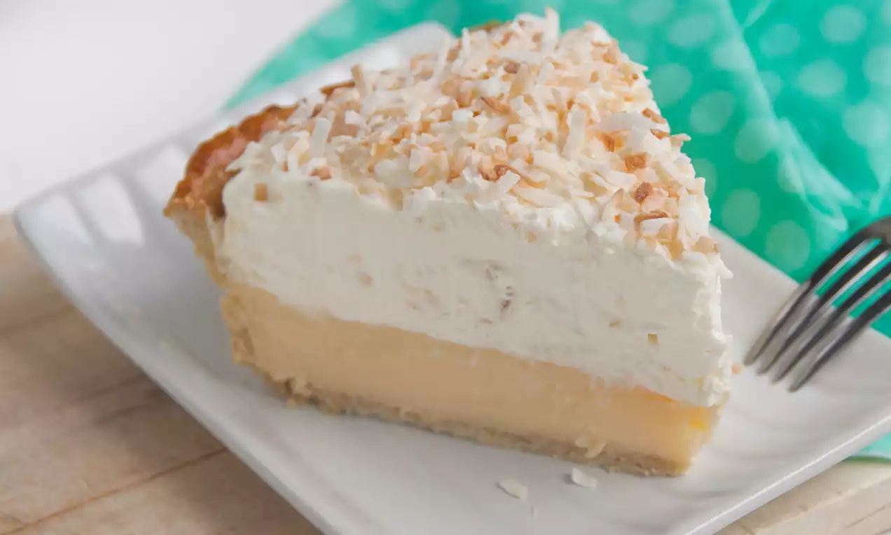 Part de tarte à la crème de coco avec une base dorée, garnie de crème fouettée blanche et de copeaux de noix de coco légèrement grillés