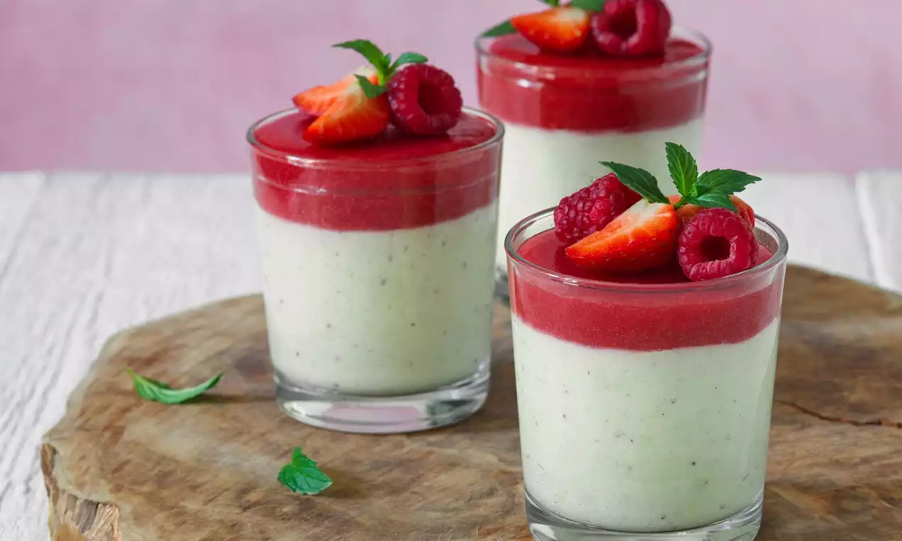 Svetlo krémové flameri s jemnými čiernymi bodkami, sýtou červenou ovocnou vrstvou, ozdobené jahodami, malinami a lístkami mäty v skle