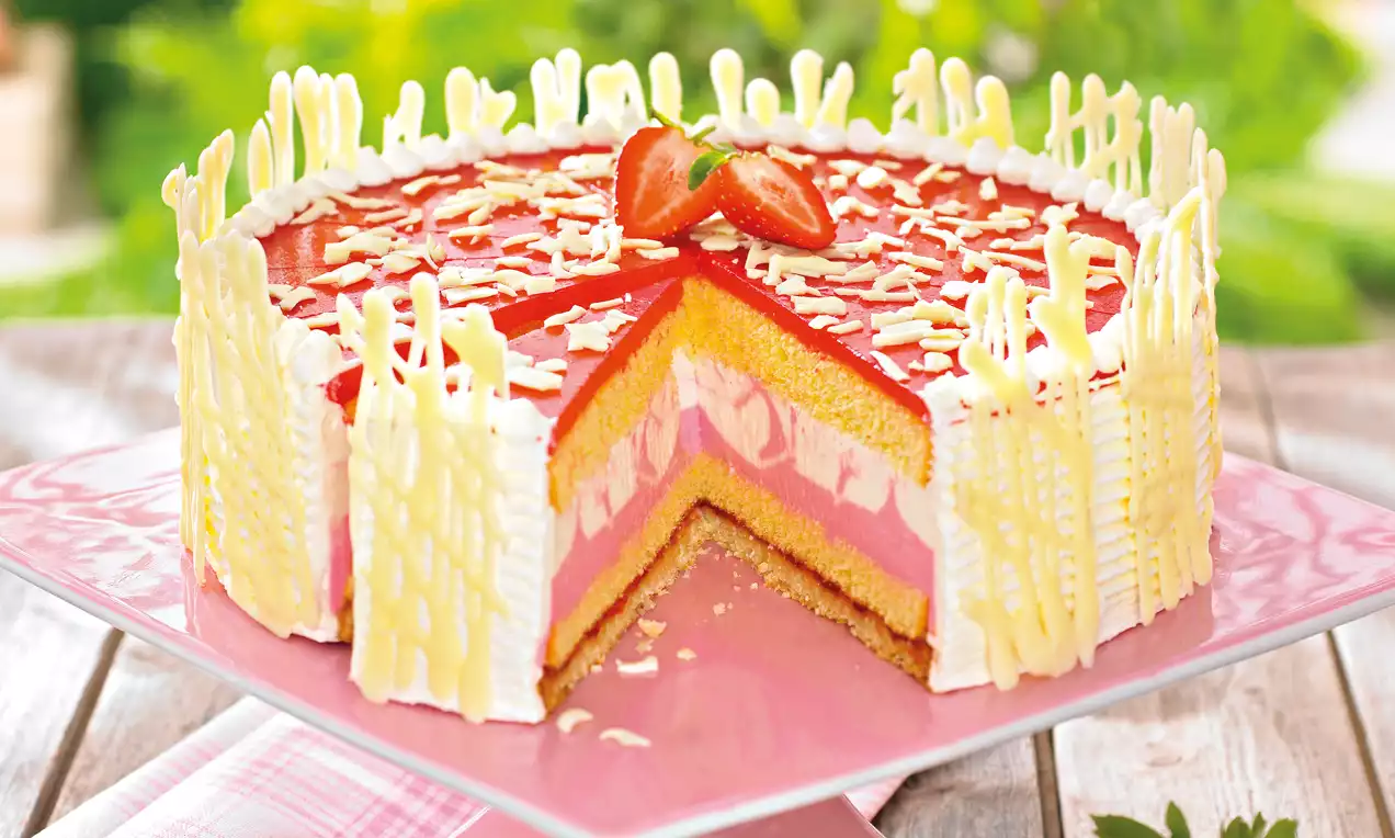 Okrugla torta s višeslojnim žutim i ružičastim nadjevom, premazana glatkom crvenom glazurom, ukrašena bijelom čokoladom i jagodom na vrhu