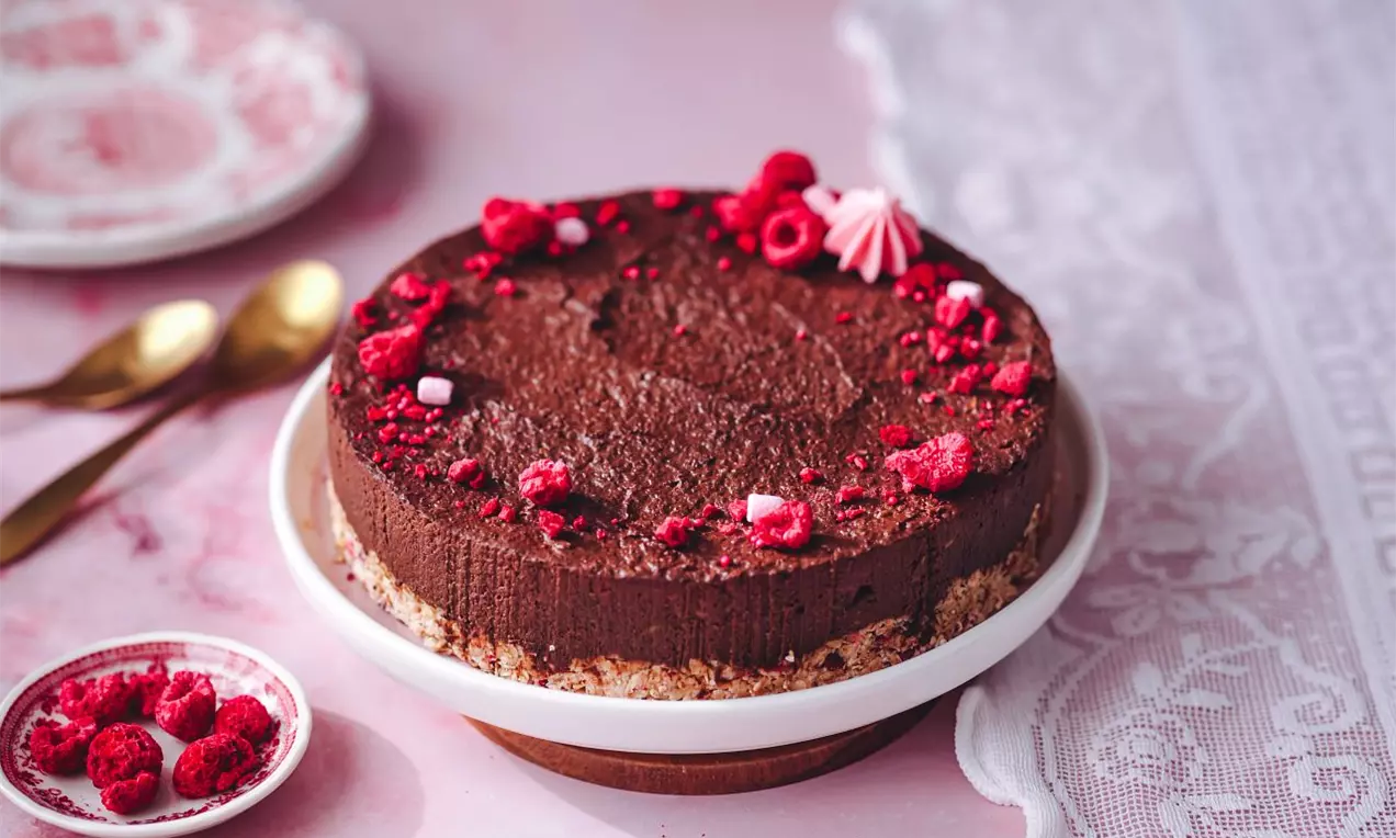 Čokoládová nepečená torta na svetlom korpuse zdobená mrazom sušenými malinami na ružovej pracovnej doske