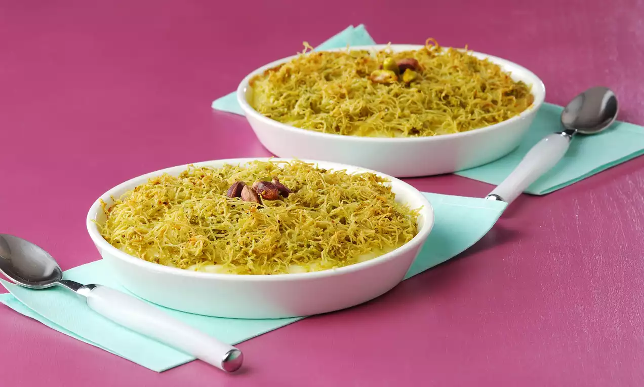 Pembe bir zeminde, beyaz yuvarlak kaselerde sunulan altın sarısı tel kadayıflı tatlılar, üzeri fıstıklarla süslenmiş şekilde öne çıkıyor