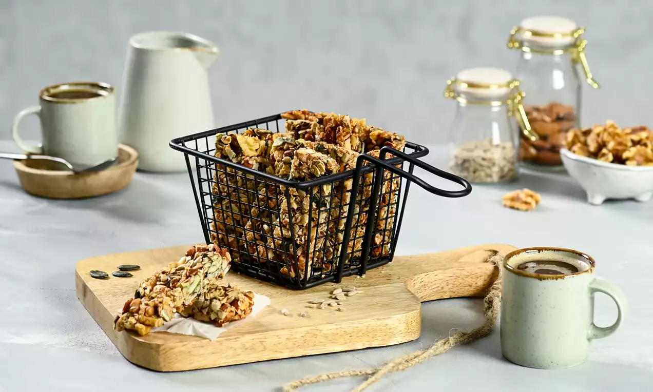 Barres dorées aux noix de Grenoble et graines mêlées, disposées dans un panier métallique noir sur une planche en bois clair
