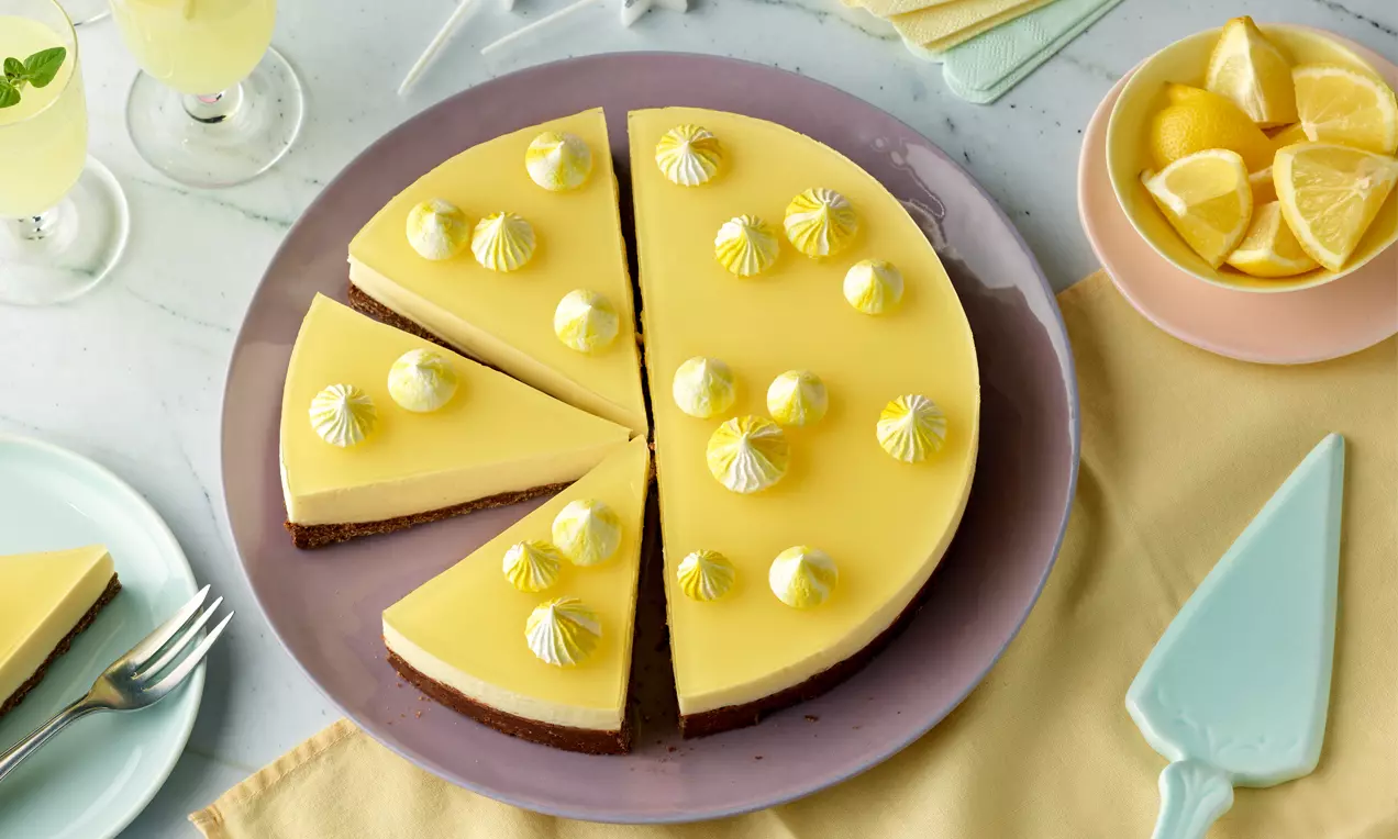 Gelbe Limoncello-Torte mit glänzendem Guss, dekoriert mit weißen und gelben Baisertupfen, auf einem Teller in Pastellfarben angerichtet
