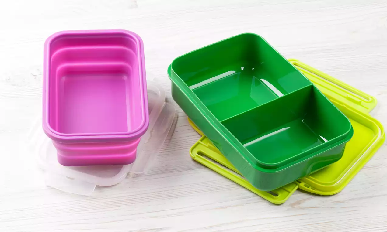 Pink and green plastic containers with divided compartments, glossy surfaces, and matching lids arranged on a light wood surface