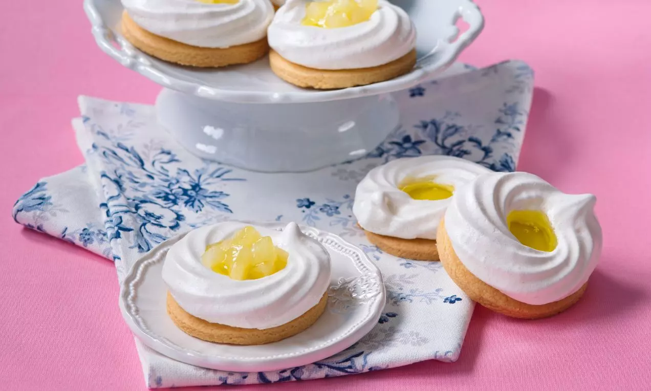 Linecká kolečka se světlým krémovým sněhovým věnečkem a žlutou marmeládou uprostřed servírovaná na bílých talířích na růžovém ubrusu