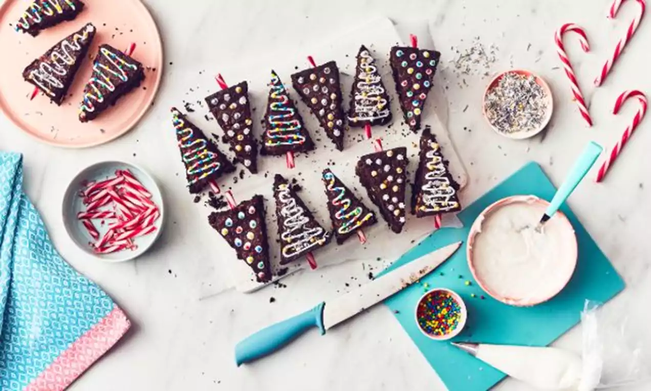 Christmas tree brownies shaped as triangles with colorful icing, sprinkles, and candy canes as stalks on a light marble surface