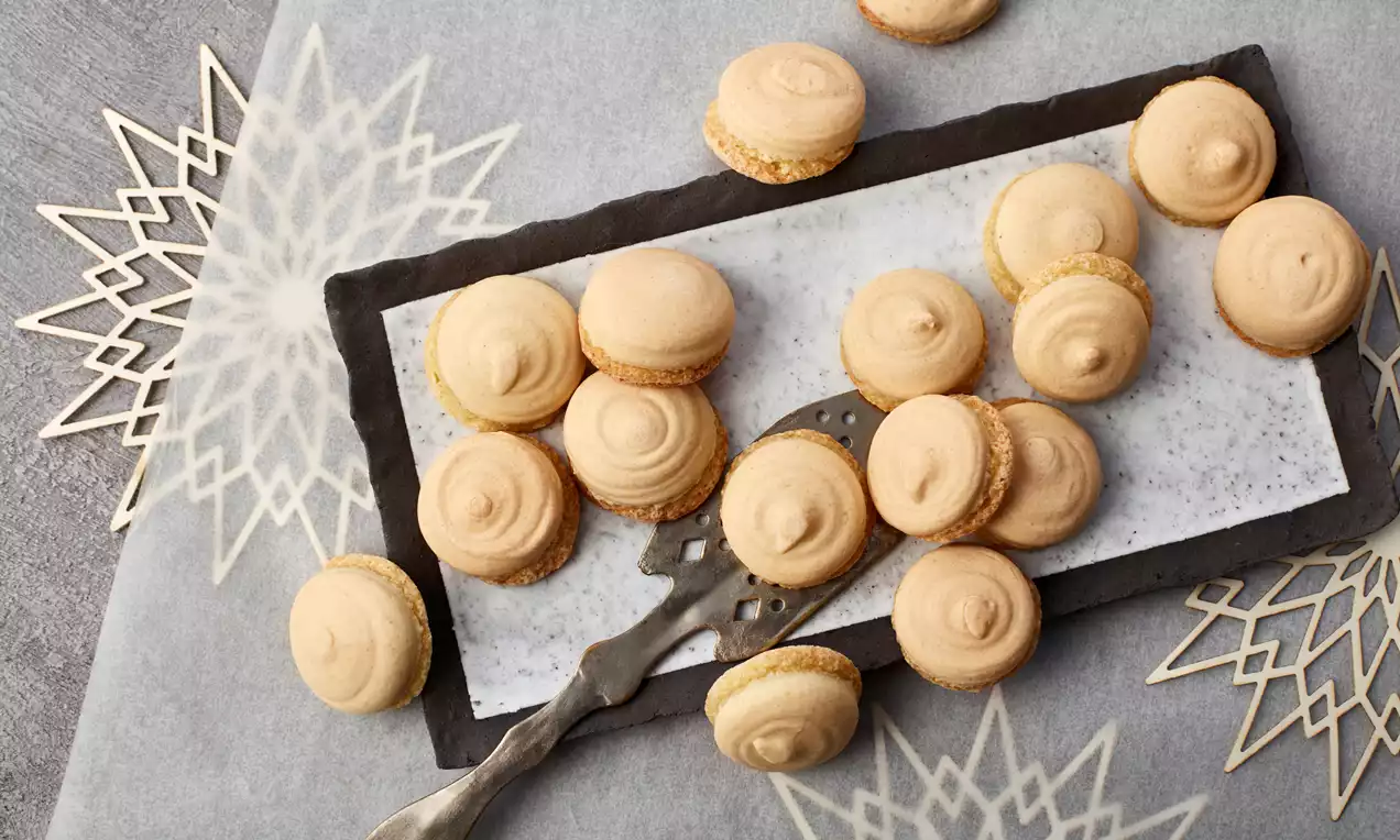 Hellgoldene Anisplätzchen mit glatter Oberfläche und feinporiger Textur auf einem rechteckigen weißen Teller mit Metallpalette eingerückt