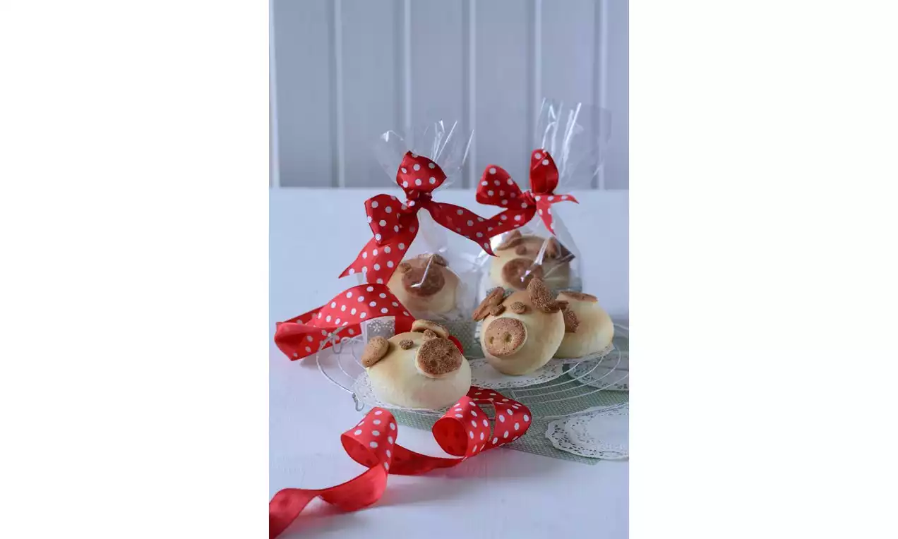 Světle žluté kulaté sušenky s hnědými mandlovými kousky na skleněném talíři, balené v průhledném sáčku s červenou puntíkovanou stuhou
