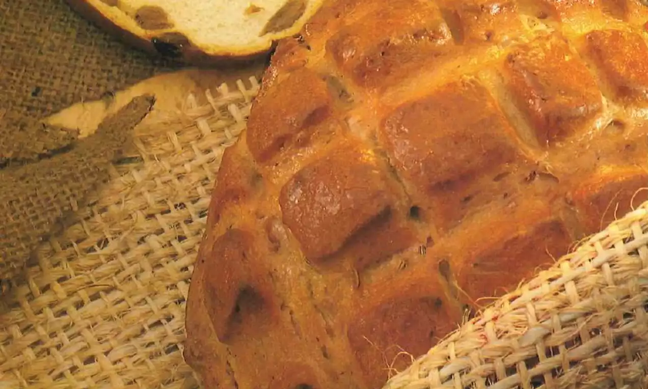 Goudbruin gevlochten brood met een glanzende korst op een rustieke jute ondergrond, met een opengesneden plak met stukjes rozijn