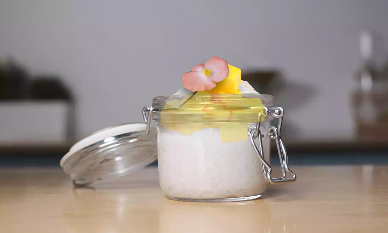 Tapiokový puding v priehľadnom zaváracom pohári, ozdobený kúskami žltého manga, kokosovými lupienkami a jemným ružovým kvetom