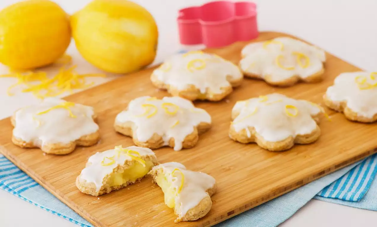 Pop tarts en forme de fleur dorées aux bords croustillants, glacées au sucre blanc et garnies de zestes de citron vibrant sur une planche en bois