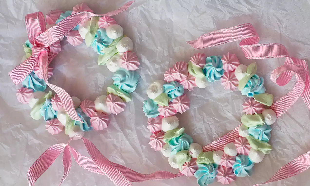 Dva venčeky z pastelových pusiniek v ružovej, modrej a zelenej, ozdobené ružovými stuhami na jemnom vrásčitom papierovom podklade