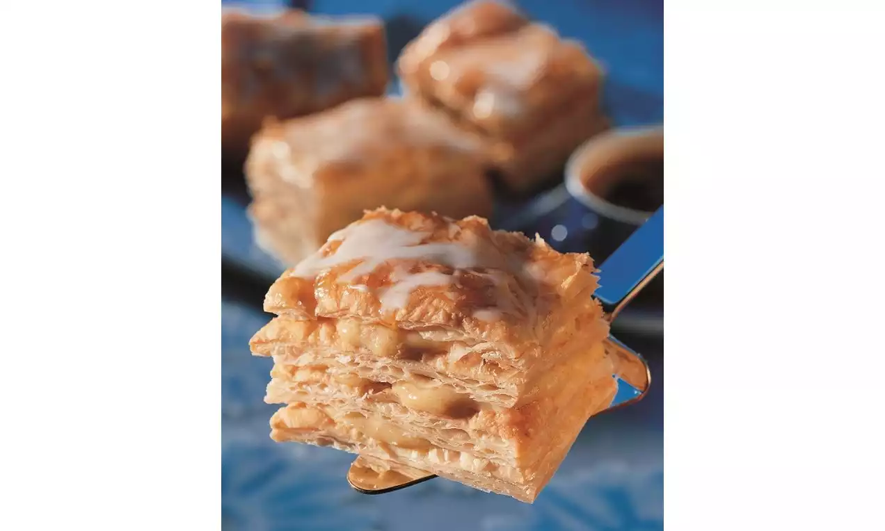 Kat kat yumuşak milföy hamuru arası karamelli dolgu, üzerinde beyaz glaze dokunuşuyla mavi tabak fonunda yakından çekilmiş