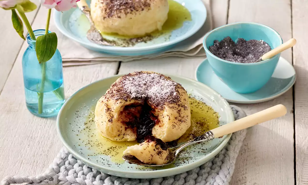 Germknödel mit heller, weicher Oberfläche, bestreut mit Mohn und Puderzucker, angerichtet auf einem Teller mit flüssiger Butter und aufgeschnitten